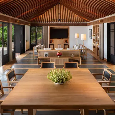 Amanoi dining pavilion with wooden table, chairs, and open doors overlooking verdant surroundings.