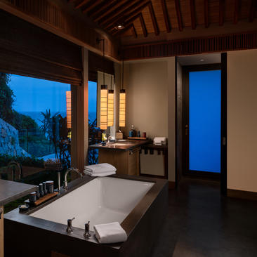 Principal bedroom with freestanding bathtub at Amanoi, evening light through large windows overlooking landscape.