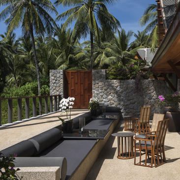 安缦璞瑞度假村的露台，配有木制座椅、石墙和棕榈树景观。