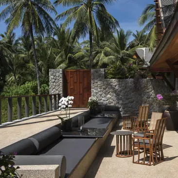 Waterfront terrace at Amanpuri with teak loungers, slate pool edge, and coconut palms.