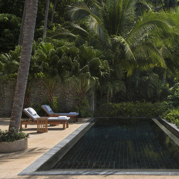 安缦璞瑞度假村泳池旁，白色躺椅坐落在棕榈树浓荫下。