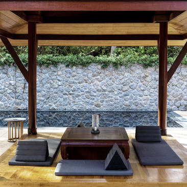 Wooden pavilion with stone wall backdrop and low seating at Amanpuri.