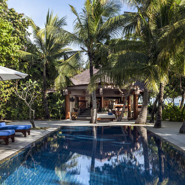 Swimming pool surrounded by palm trees at Amanpulo, with open-sided pavilion and loungers.