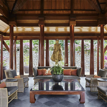安缦璞瑞度假村宽敞的木制休闲厅，落地窗框绿树景致，配有传统家具。