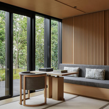 アマン京都のリゾートの客室。木製の縦格子パネルに囲まれた、ミニマルなシーティングエリア。大きな窓から緑が見える。