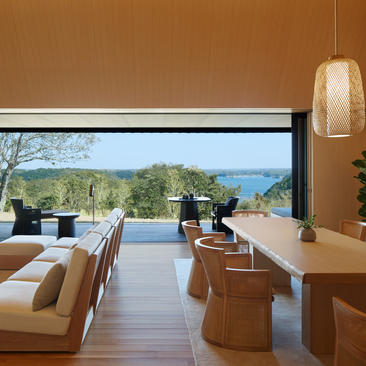 Amanemu resort interior with open terrace overlooking bay and forested coastline, featuring minimalist wooden furniture and warm earth tones.