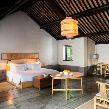 法云安缦度假村的房间，配有木质天花板、米色床铺和绿色小桌。