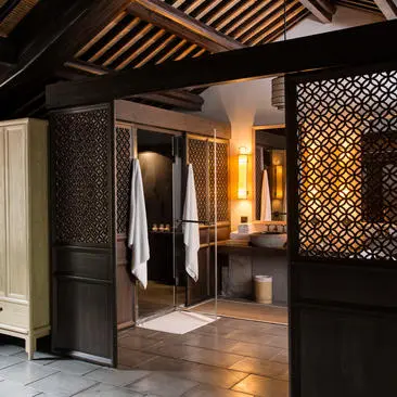 Amanfayun villa bathroom with wooden ceiling beams, stone flooring, and geometric latticed screens.