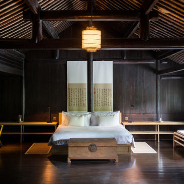 法云安缦度假村卧室内，木制平台床铺置于宽敞空间中，顶部悬挂温暖吊灯。