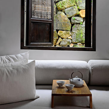 法云安缦度假村的宽敞起居区，配有灰色沙发、白色靠枕和木制茶几，窗外可见传统建筑。
