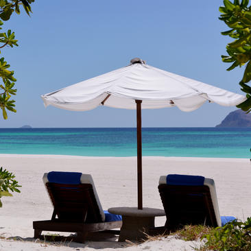 Deux chaises longues noires sous un parasol blanc sur la plage de sable blanc d'Amanpulo, avec turquoise lagon en arrière-plan.