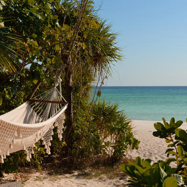Hamac blanc suspendu entre palmiers face à la plage de sable blanc et mer turquoise à Amanpulo.
