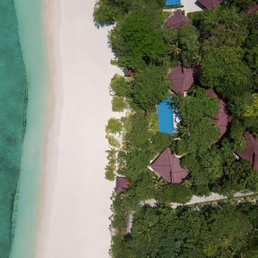 Aerial view of a three-bedroom villa nestled among tropical vegetation at Amanpulo resort, with turquoise waters and white sand beach.