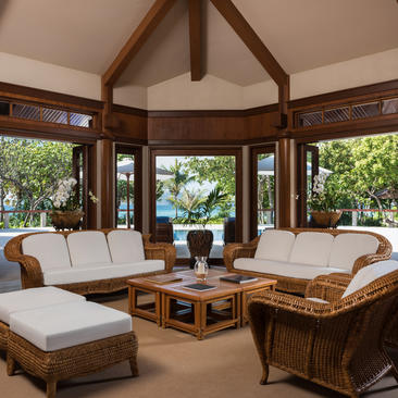 Sala de estar de villa de dos dormitorios en Amanpulo, con sofás de ratán, vigas de madera y vistas al jardín.