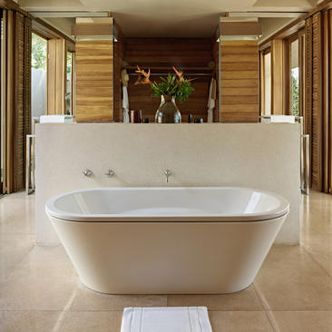 Freestanding white bathtub in a suite bathroom at Amanwella, with wooden wall panelling and dual mirrors.