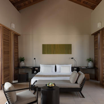 Amanwella suite bedroom with olive-green headboard, wooden ceiling, and neutral furnishings.