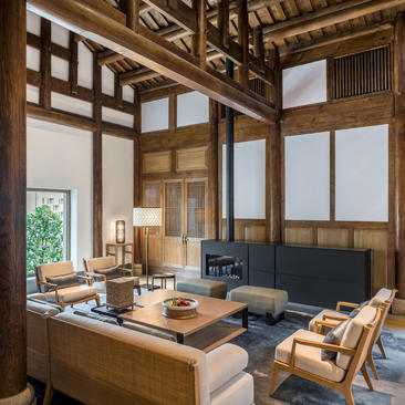 Living area in a villa at Amanyangyun, with wooden lattice screens, desk and seating beneath exposed timber beams.