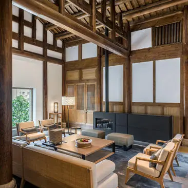 Living area in a villa at Amanyangyun, with wooden lattice screens, desk and seating beneath exposed timber beams.