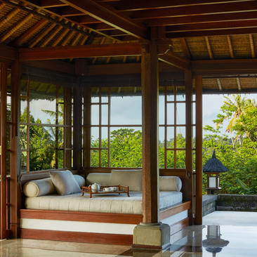 Living area in Amandari suite with cushioned daybed, wooden shutters, and views to terraced landscape.
