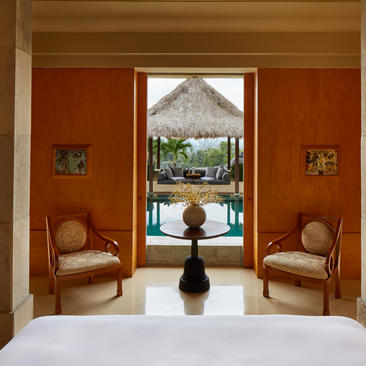 Borobudur Pool Suite sitting area with terracotta walls, two wooden chairs, and arched doorway opening to garden at Amanjiwo.