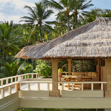 Terrace of a garden suite at Amankila resort, with thatched roof pavilion and tropical palms.