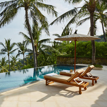 Wooden sunloungers beneath a canopy overlook an infinity pool at Amankila resort.