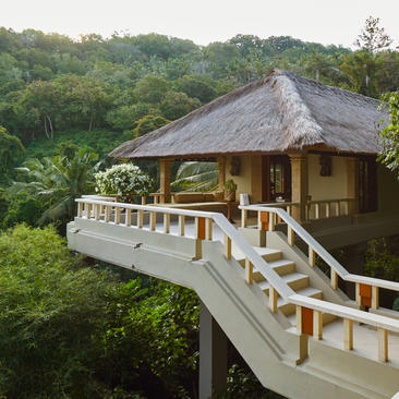 Amankila treehouse suite with thatched roof and wooden deck overlooking lush forest canopy.