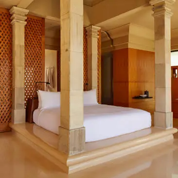 Kamar tidur berkolom dengan tempat tidur berkanopi dan pintu kayu di Amanjiwo resort.