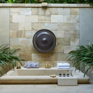 Outdoor bathtub set against stone wall with circular mirror and potted plants at Amanjiwo resort.