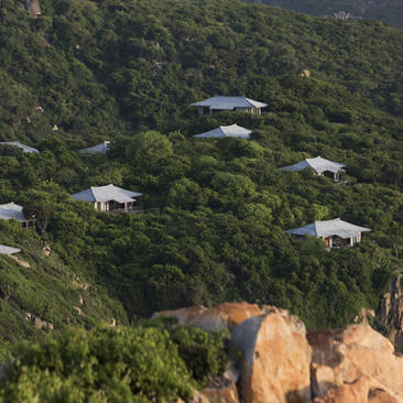 Aerial view of Amanoi's pavilions scattered across verdant hillside with coastal cliffs.