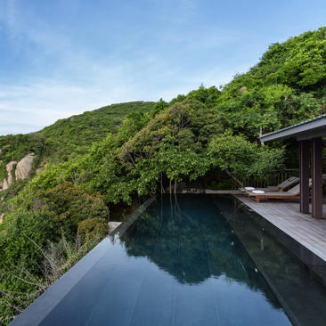Infinity swimming pool overlooking verdant hillside at Amanoi, reflecting clear sky and surrounding landscape.
