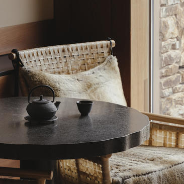 Woven basket chair beside black round table at Amangani, with mountain views through window.