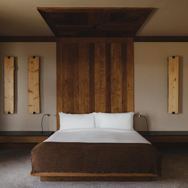 Sena Suite bedroom at Amangani with wooden bed frame and white bedding, flanked by vertical wall sconces.