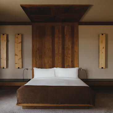Principal bedroom in the Shoshone Suite at Amangani, featuring a wooden bed frame with white bedding and minimalist wall sconces.