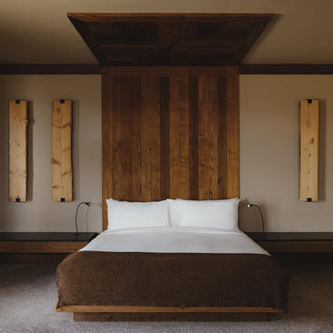 Principal bedroom at Amangani with dark wood bed frame and white bedding, flanked by wall sconces.