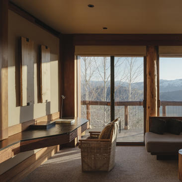 Sunlit principal bedroom at Amangani with mountain views through floor-to-ceiling windows and warm wooden finishes.