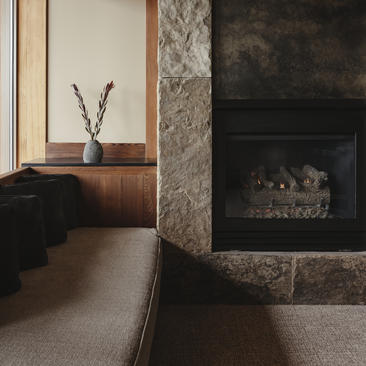 Fireplace with stone surround and lit logs, wooden shelf with dried grasses in vase at Amangani.