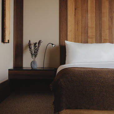 Bedside table with vase and reading lamp beside bed with white pillows at Amangani.