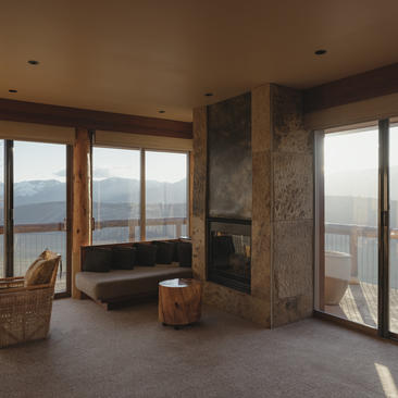 Amangani suite with floor-to-ceiling windows framing mountain and valley views, featuring a stone fireplace and contemporary furnishings.