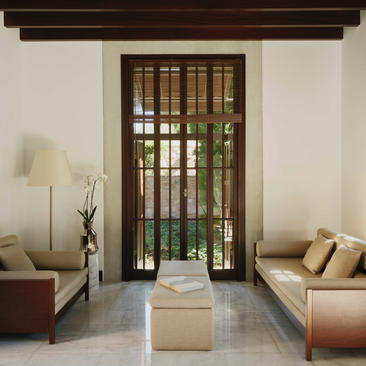Deluxe Sea View Pavilion lounge at Amanruya with symmetrical seating, dark wooden doors opening to sea views, and natural light filtering through.
