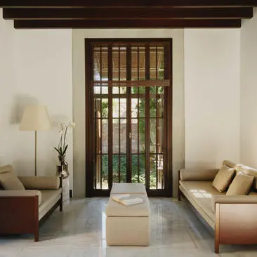 Deluxe Sea View Pavilion lounge at Amanruya with symmetrical seating, dark wooden doors opening to sea views, and natural light filtering through.