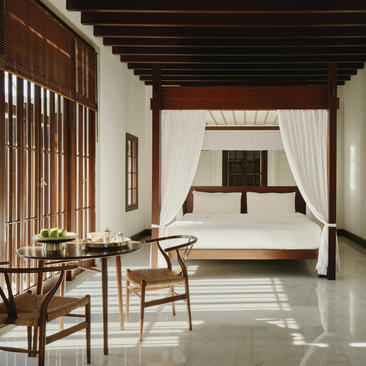 Deluxe sea view bedroom at Amanruya with canopied bed, wooden seating area and terracotta ceiling beams.
