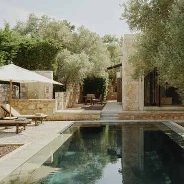 Exterior pool at Amanruya with stone pavilion, olive trees and seating area reflected in still water.