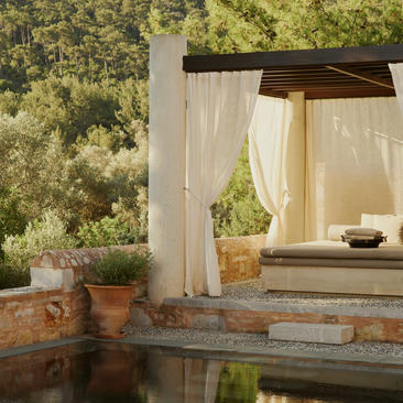Poolside pavilion at Amanruya with draped curtains overlooking garden views and terracotta planters.