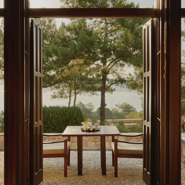 Deluxe Sea View Pavilion balcony at Amanruya, Turkey, with open wooden doors framing a dining table and coastal views beyond.