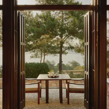 Deluxe Sea View Pavilion balcony at Amanruya, Turkey, with open wooden doors framing a dining table and coastal views beyond.