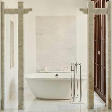 Amanruya Pool Suite bathroom with freestanding bathtub, marble walls, and floor-to-ceiling windows.