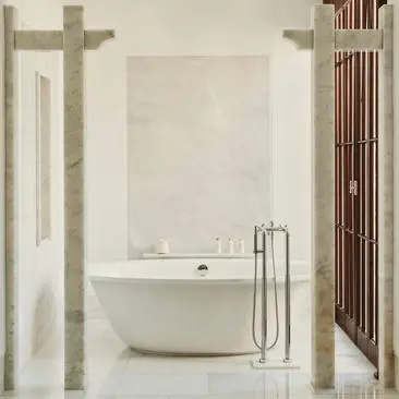 Amanruya Pool Suite bathroom with freestanding bathtub, marble walls, and floor-to-ceiling windows.