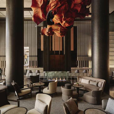 アマン ニューヨークのラウンジ。天井から垂れ下がる赤と金色の装飾が施された大きな空間。グレーのソファとテーブルが配置されている。