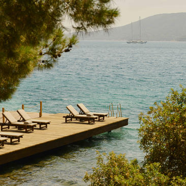 Wooden jetty with sunloungers extending into turquoise water at Amanruya, framed by pine trees.